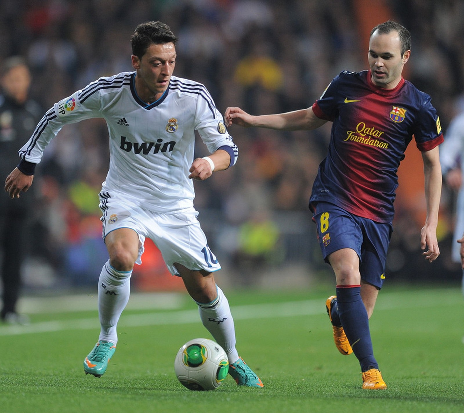 Dois jogadores de futebol estão jogando futebol em um campo de futebol (iniesta, özil)