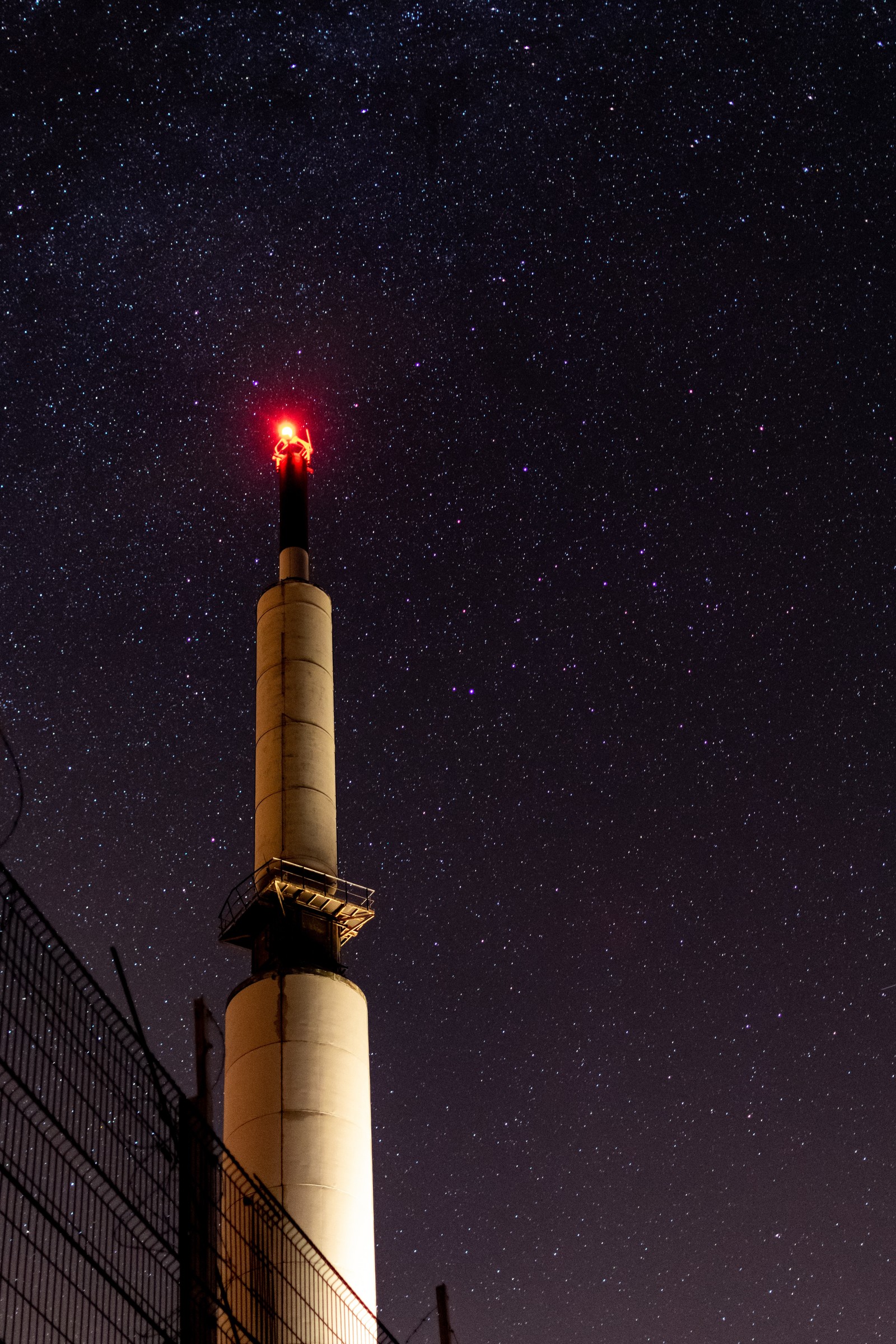 Céu estrelado com um farol e uma cerca em primeiro plano (ciência, vermelho, arquitetura, noite, farol)