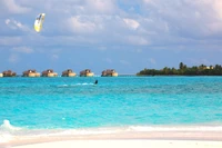 Ruhiger Karibikstrand mit Überwasser-Villen und Kite-Surfer