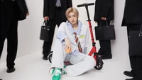 Sunghoon d'ENHYPEN pose de manière stylée sur un scooter, entouré de personnes en tenue formelle.