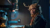 A young boy with deer antlers and a scarf, gazing curiously in a dimly lit room.