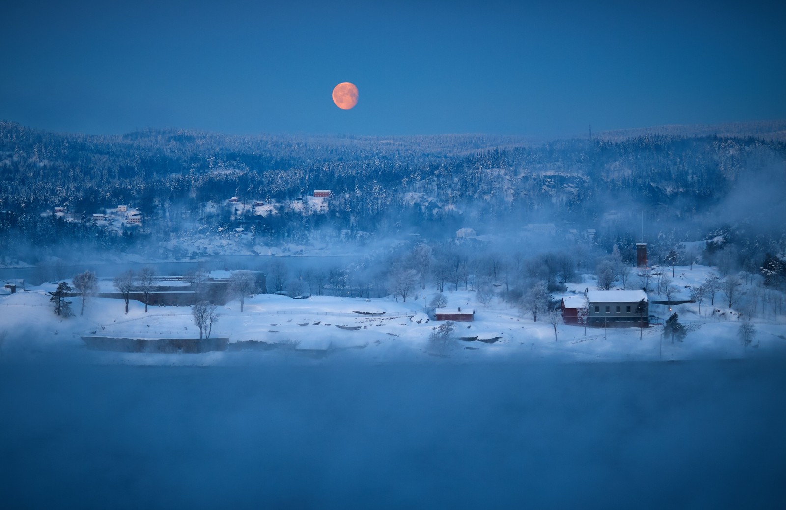 Vista de una luna llena elevándose sobre un pequeño pueblo en las montañas (azul, agua, invierno, congelación, atmósfera)