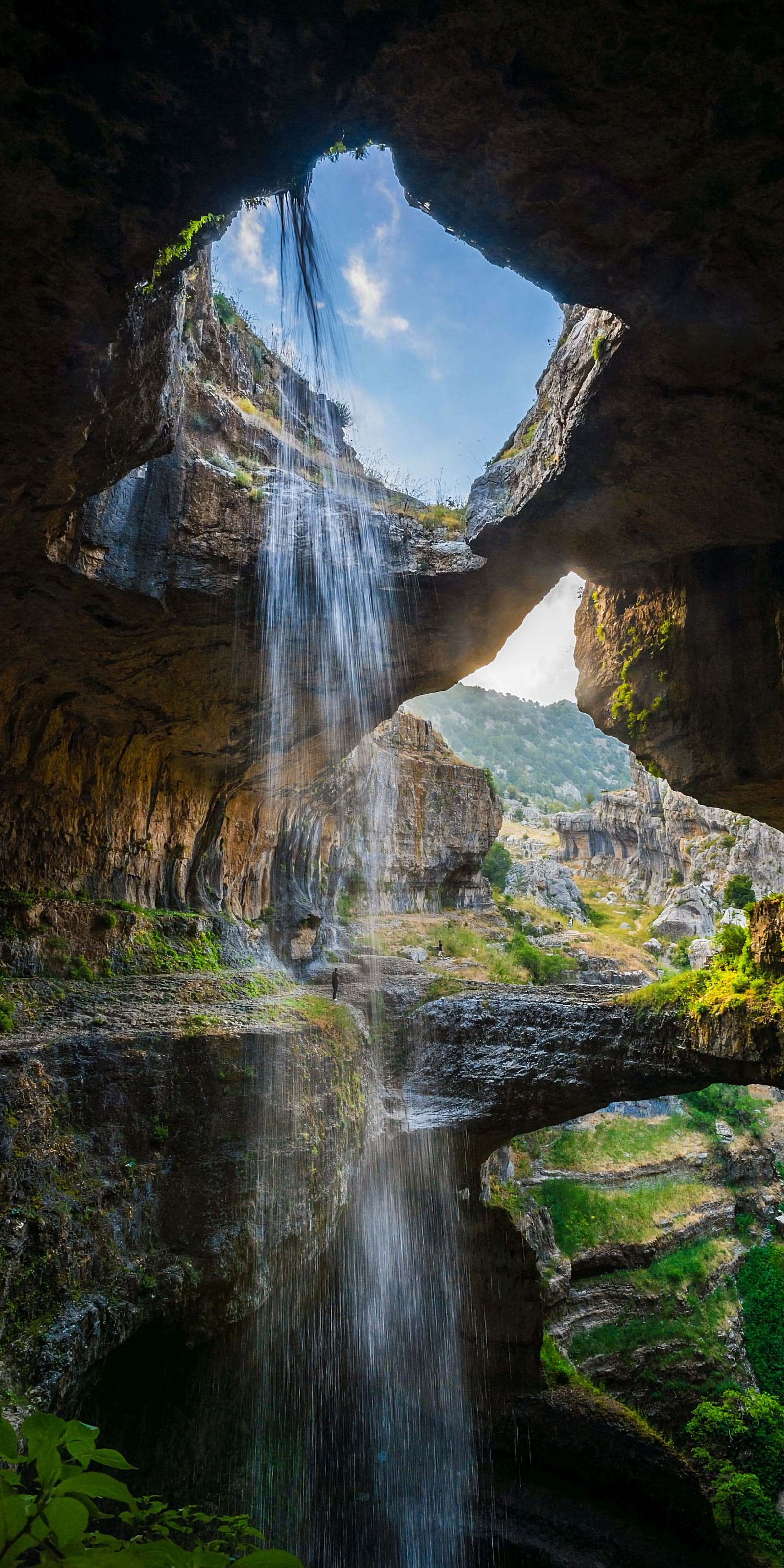 Uma vista de uma cachoeira saindo de uma caverna para uma floresta (anime, natureza)