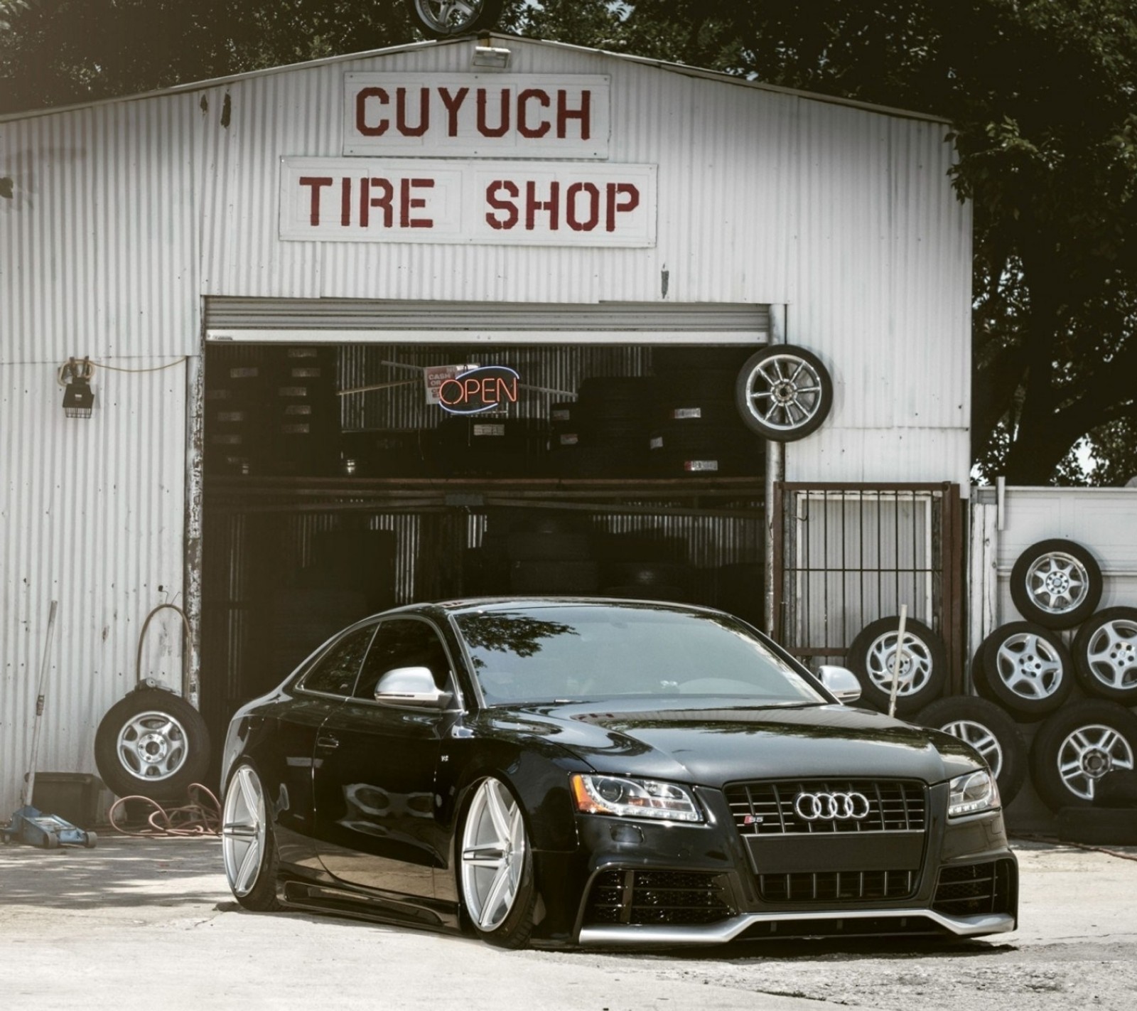 Un coche audi estacionado frente a un taller de neumáticos (audi, negro, coche, oscuro, vidrio)