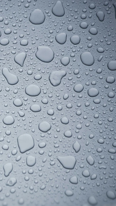 Macro shot of raindrops on a surface, showcasing varying sizes and patterns of water droplets.