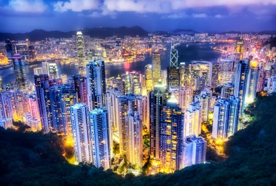 Vista aérea vibrante do horizonte da cidade de Hong Kong ao pôr do sol, exibindo arranha-céus e luzes noturnas refletindo no rio.