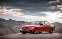 Elegante sedán rojo Mercedes-Benz E-Class posicionado contra un dramático fondo montañoso.