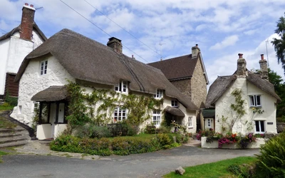 Charmantes Reetdachhaus, umgeben von üppigem Grün und lebhaften Blumen, das klassische mittelalterliche Architektur in der englischen Landschaft zeigt.