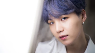 Min Yoongi (Suga) do BTS olha pensativo com uma expressão suave, exibindo seu cabelo roxo característico e um traje estiloso.