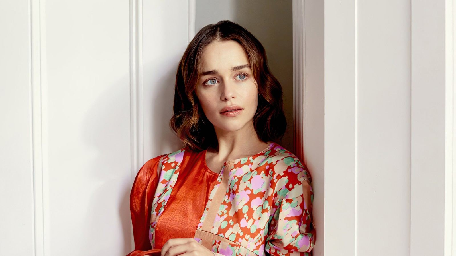 Femme girafe en robe rouge et orange appuyée contre un mur (emilia clarke, actrice, célébrité, femmes, filles)