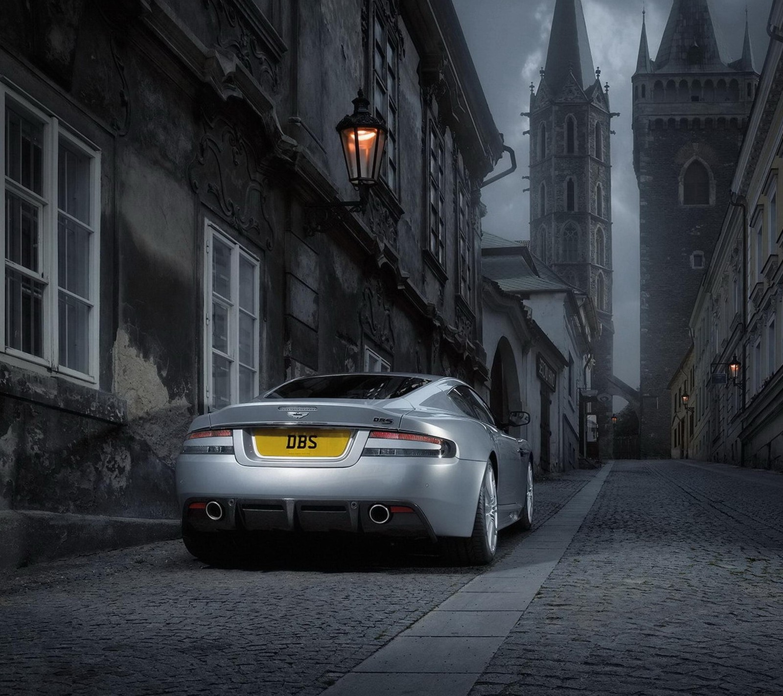 Arafed car parked on a cobblestone street in front of a tall building (aston martin, automobile, cars, dbs, fast)