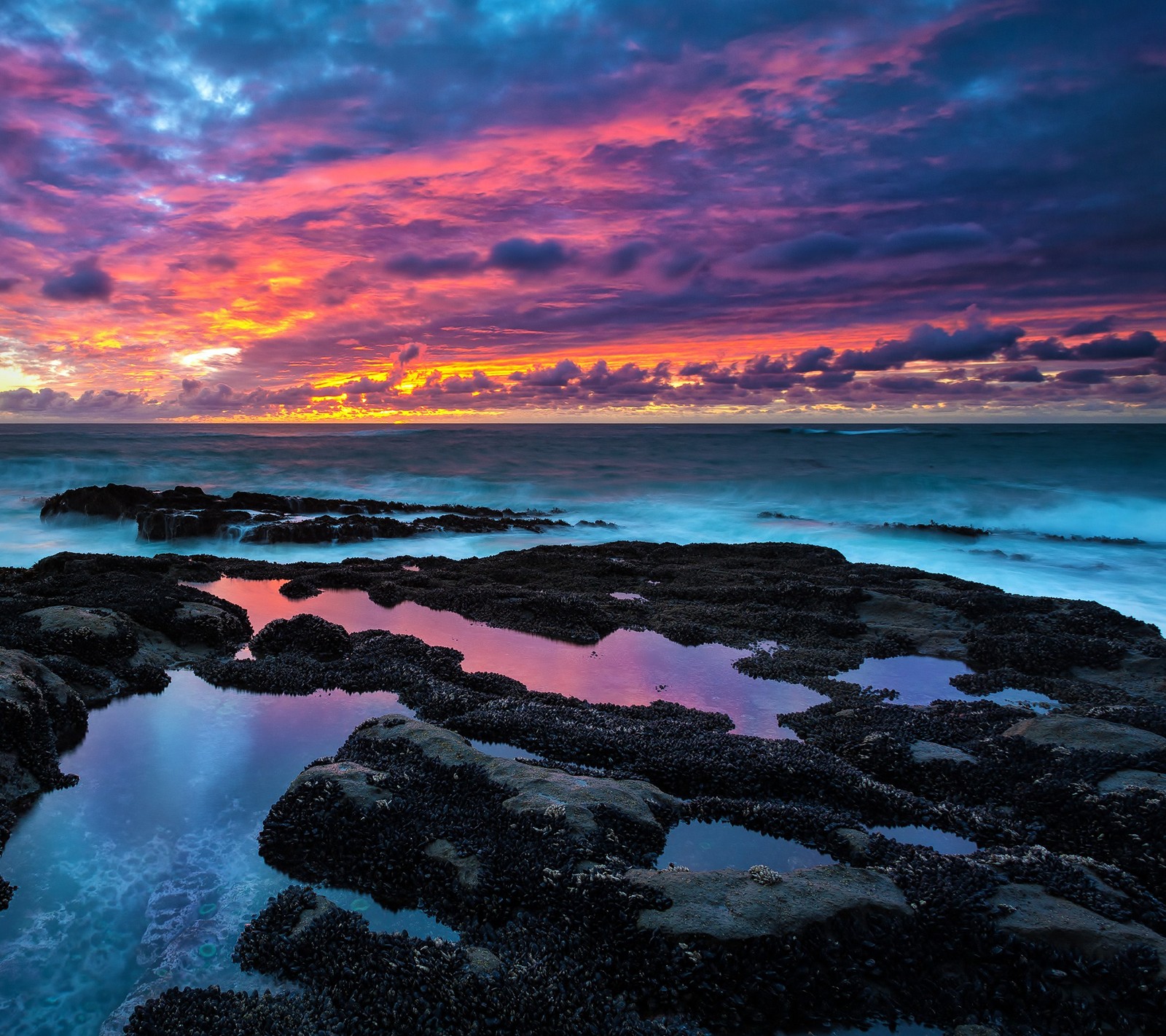 Une vue d'un coucher de soleil coloré sur l'océan avec des rochers et de l'eau (plage, nature, océan, rochers, paysage)