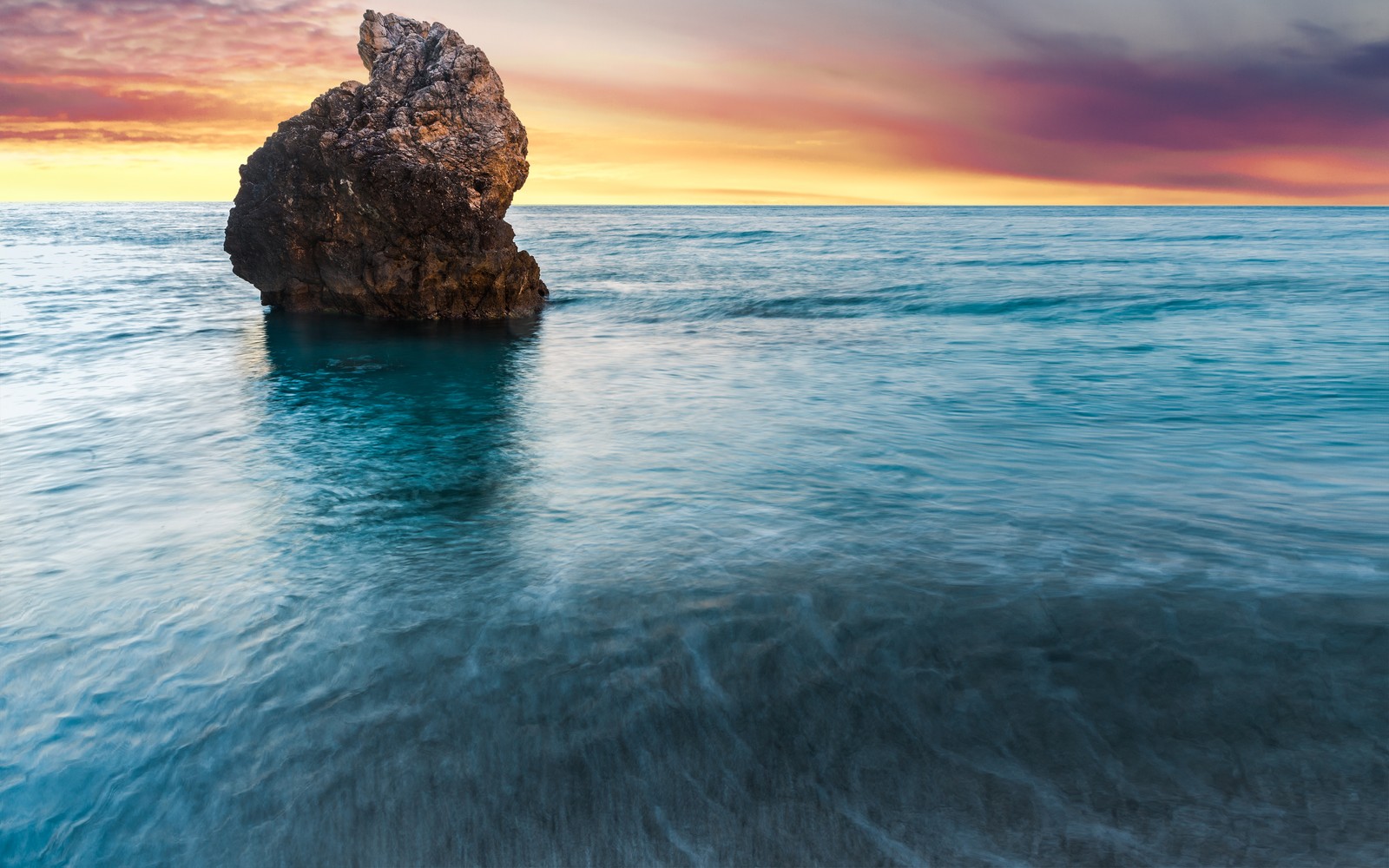 Una roca en medio del océano con un atardecer de fondo (isla lefkada, grecia, playa milos, atardecer, paisaje marino)