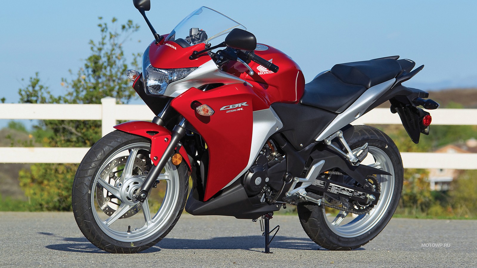 Arafed red and black motorcycle parked on the side of the road (honda motor company, fuel injection, motorcycle, honda cbr250r, car)