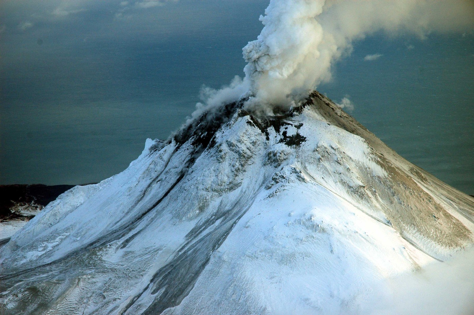 Une montagne en éruption avec un panache de fumée qui s'échappe (stratovolcan, volcan, forme glaciaire, ciel, sommet)