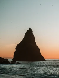 Silhouette de una pila costera contra un vibrante horizonte de atardecer