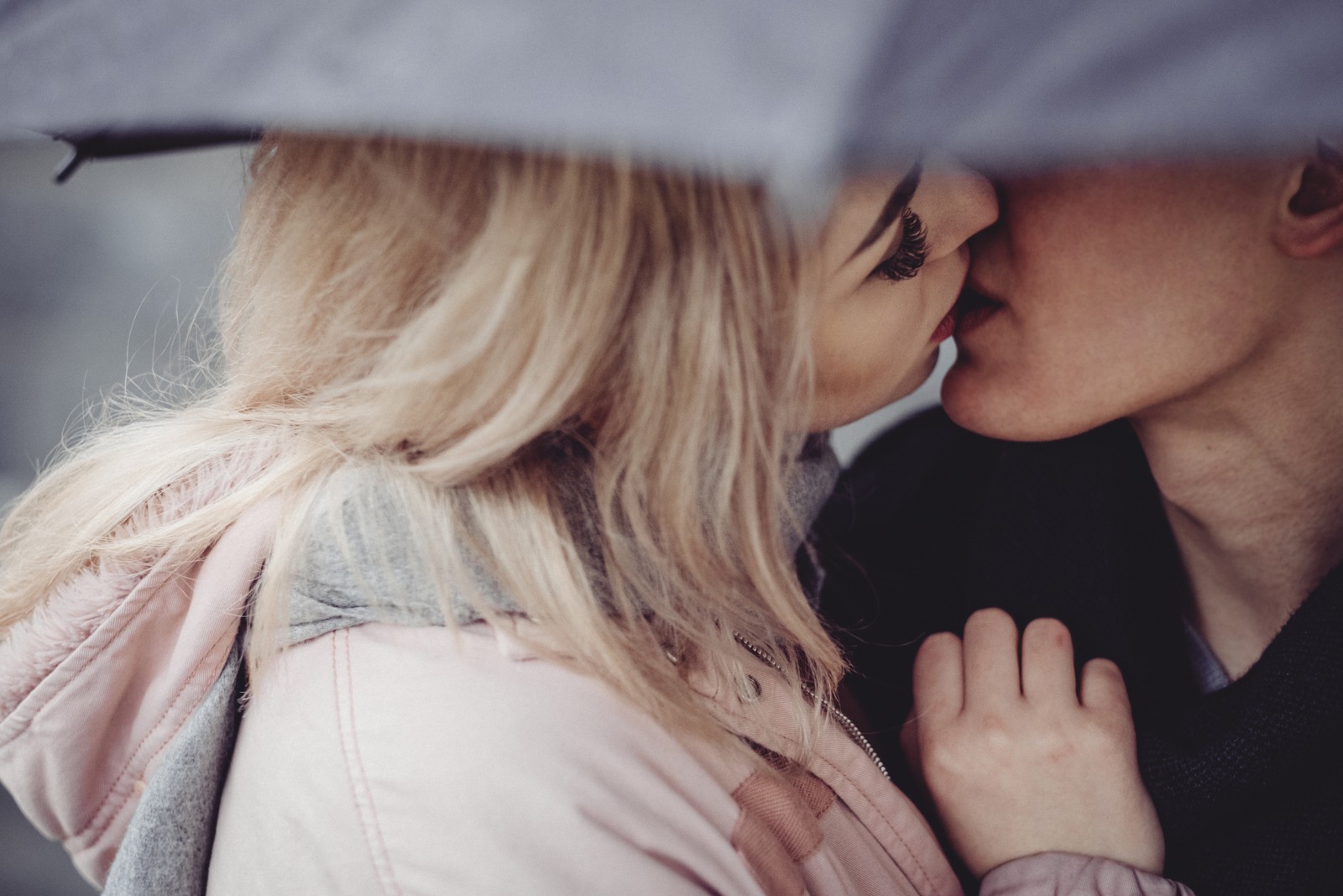 Un homme et une femme s'embrassent sous un parapluie (baiser, romance, couple, cheveux, blond)