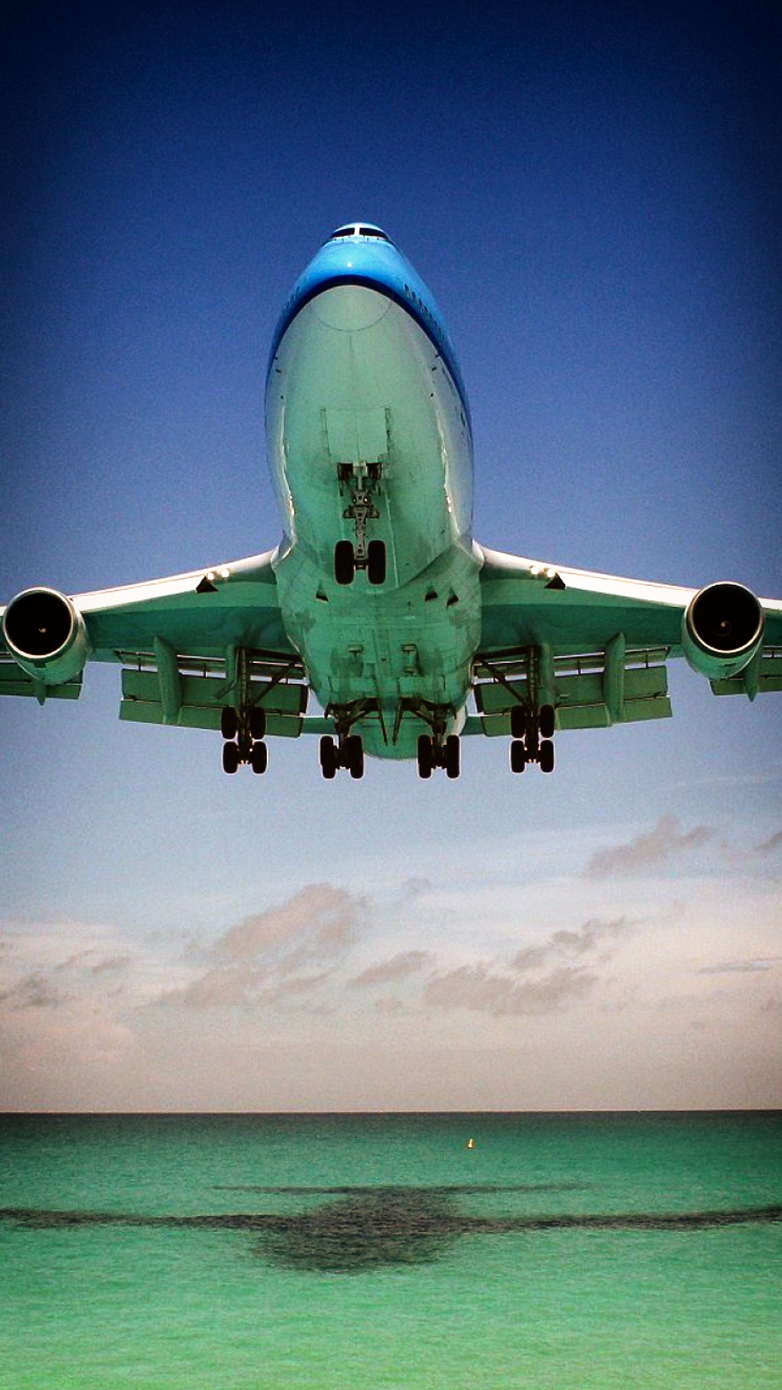 Un avion atterrissant au-dessus de l'océan avec un ciel bleu et des nuages (avion, vol, boeing 747 400, aéronef, aviation)