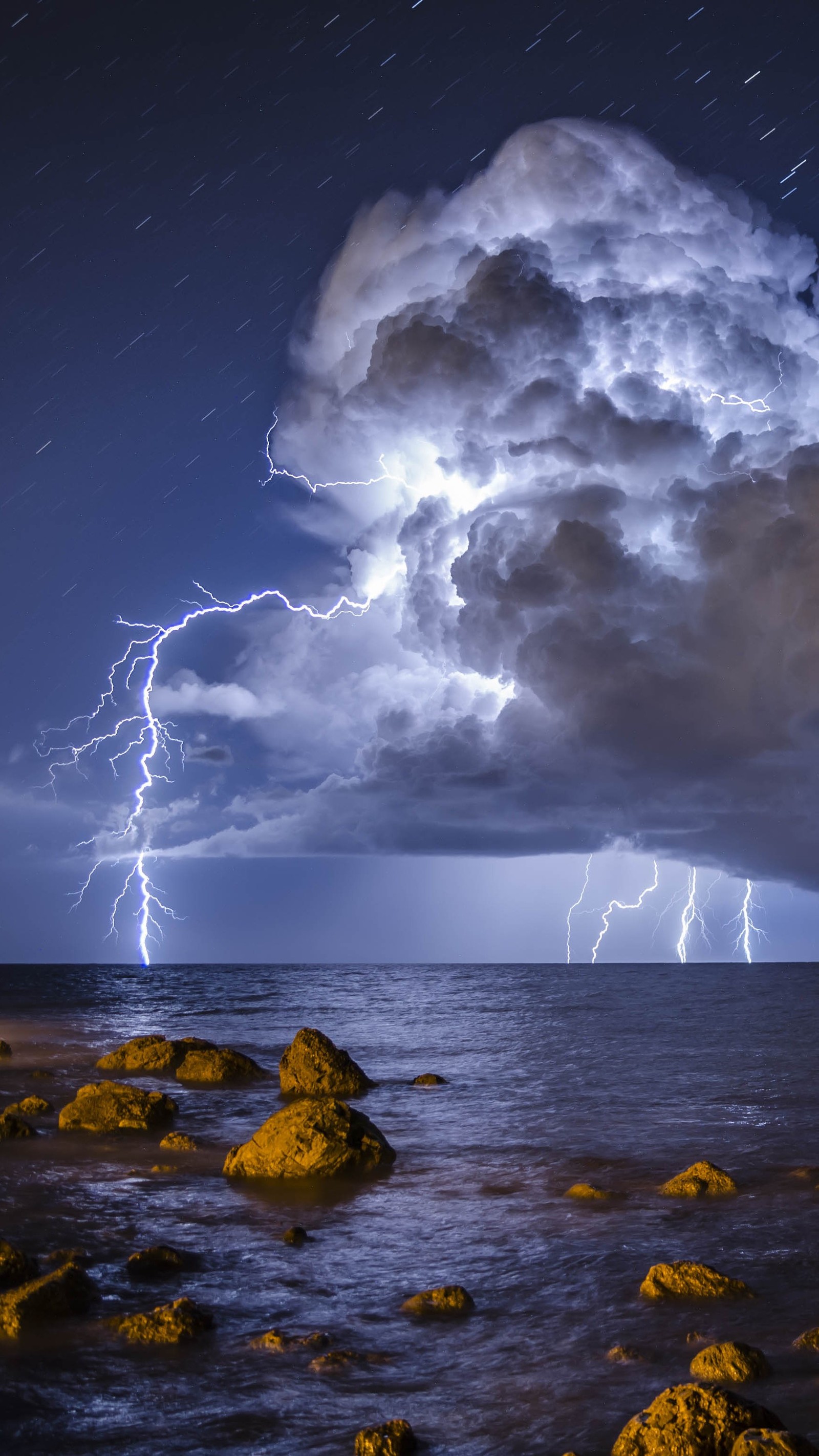 Lightning strikes over the ocean as it passes over rocks (blue, cloud, lightning, nature, sea)