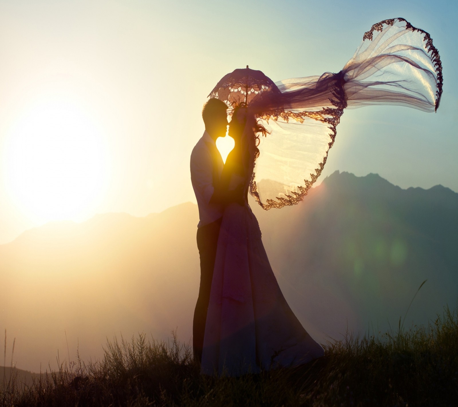 Braut und bräutigam küssen sich in den bergen bei sonnenuntergang mit einem im wind wehenden schleier (paar, umarmung, liebe, liebende)