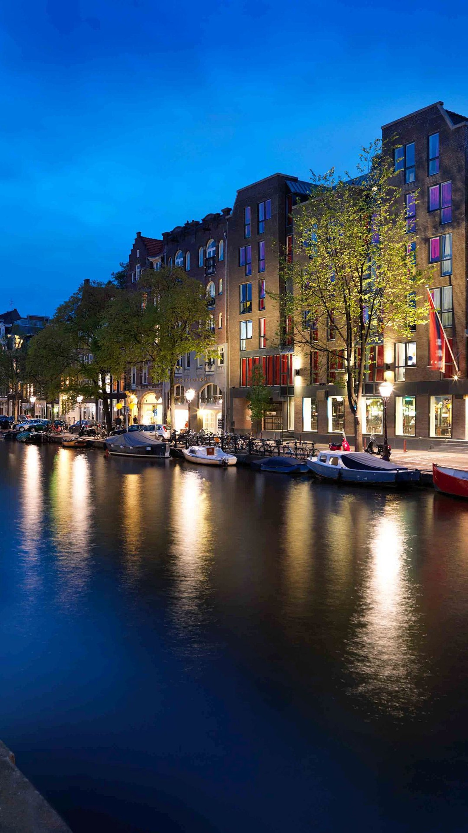 Barcos estão atracados na água em uma cidade à noite (amsterdã, amsterdam, barcos, canal, anoitecer)