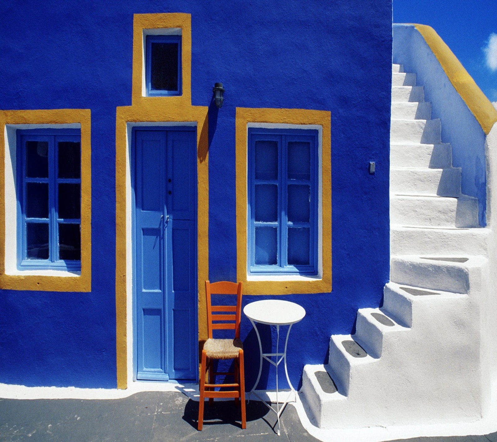 Silla y mesa afuera de un edificio azul y amarillo (hermoso, casa)