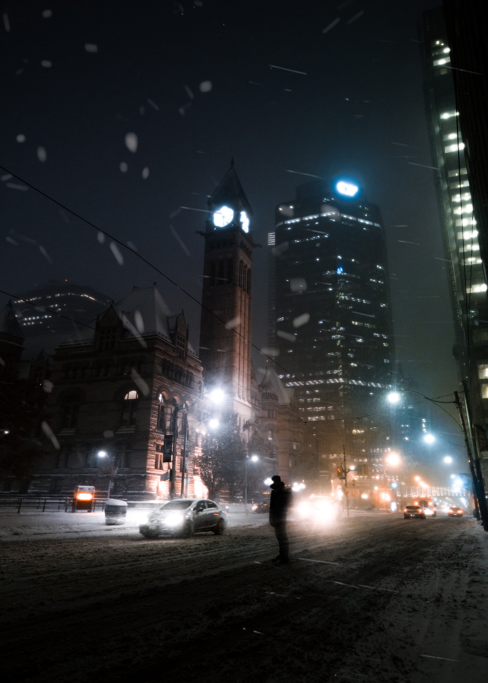 Cena noturna nevada de uma rua da cidade com uma pessoa andando na neve (arranha céus, arquitetura, luz, edifício, cidade)