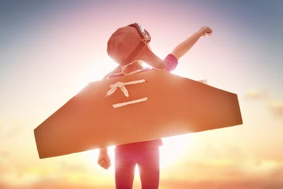 Niño con alas de cartón alcanzando el cielo, encarnando sueños de vuelo bajo la cálida luz del sol.