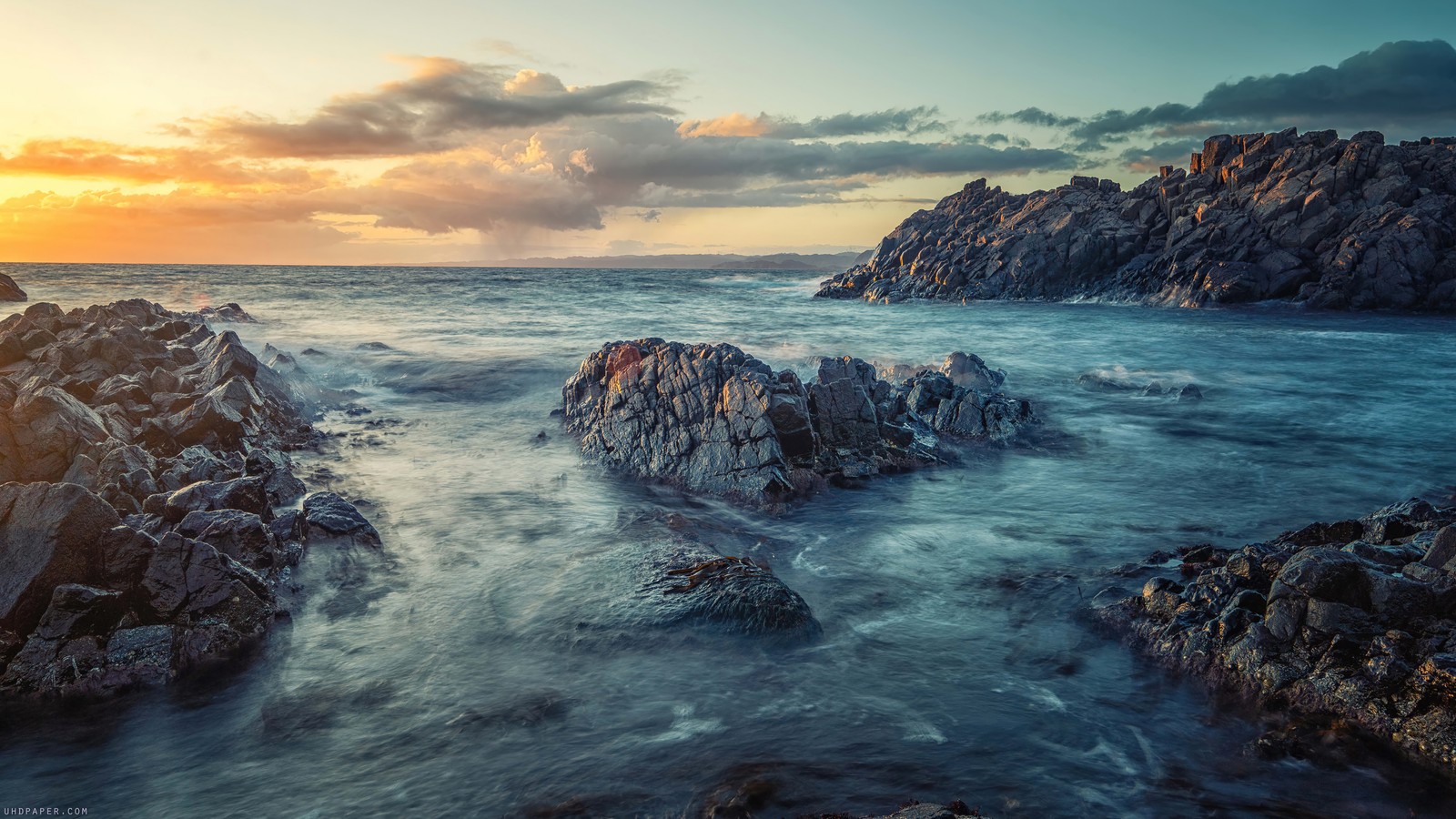 Uma vista de uma praia rochosa com um pôr do sol ao fundo (rocky, praia, por do sol, cenário)