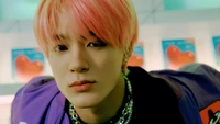 Jeno of NCT Dream with pink hair, showcasing a striking look in a vibrant setting.