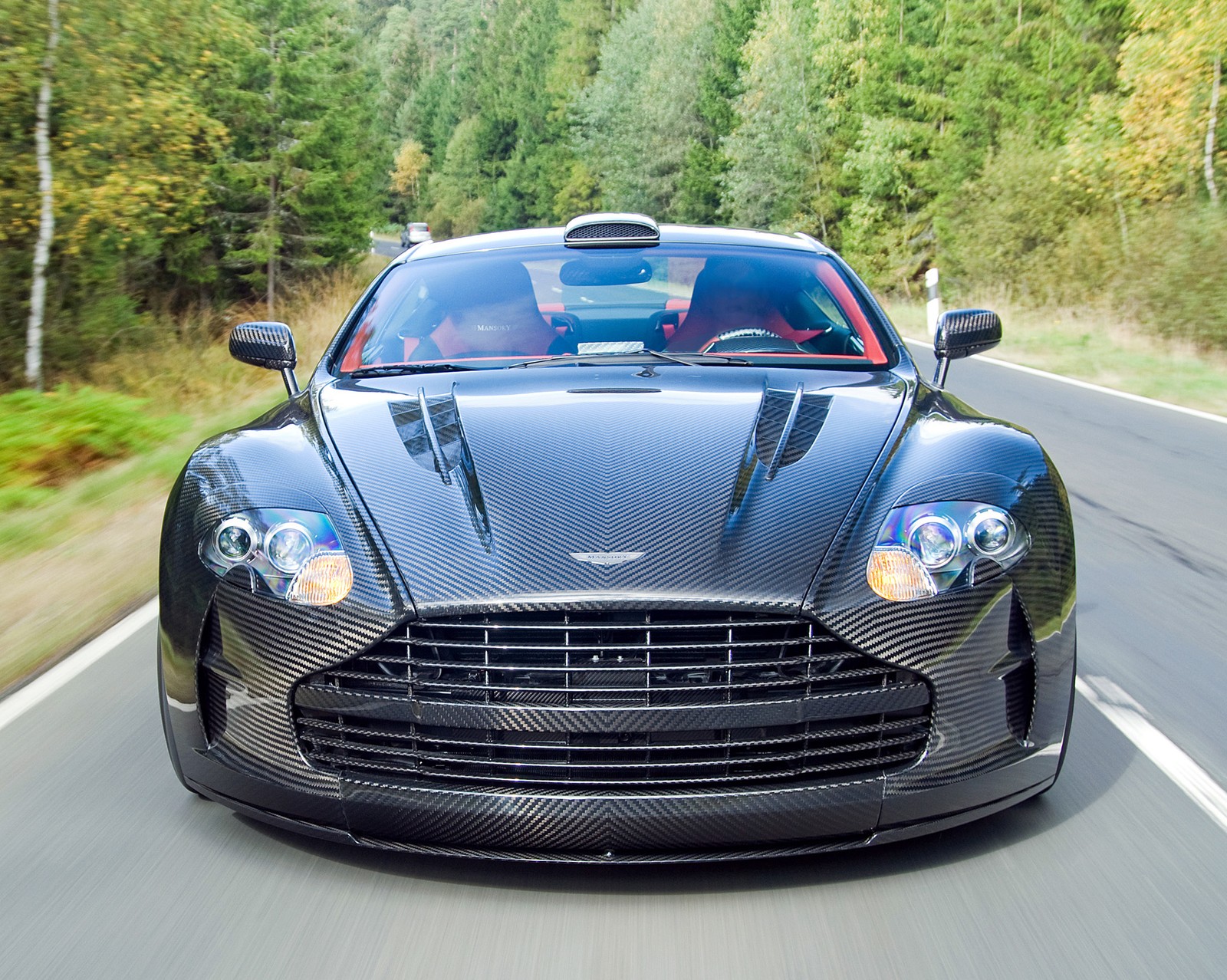 A close up of a black car driving down a road (aston, carbon, fiber, martin)