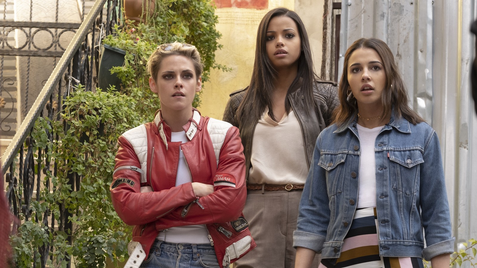 Tres mujeres están de pie en un callejón estrecho con un hombre en una chaqueta roja. (los ángeles de charlie, película, kristen stewart, naomi scott, ella balinska)