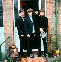 Los Beatles con trajes formales elegantes, posando en una puerta, exudando una mezcla de música y moda.