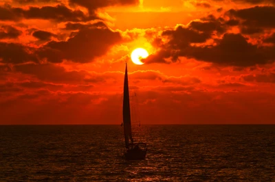 Silhueta de um veleiro contra um pôr do sol vibrante sobre o oceano, com nuvens dramáticas refletindo tons quentes de laranja e ouro.