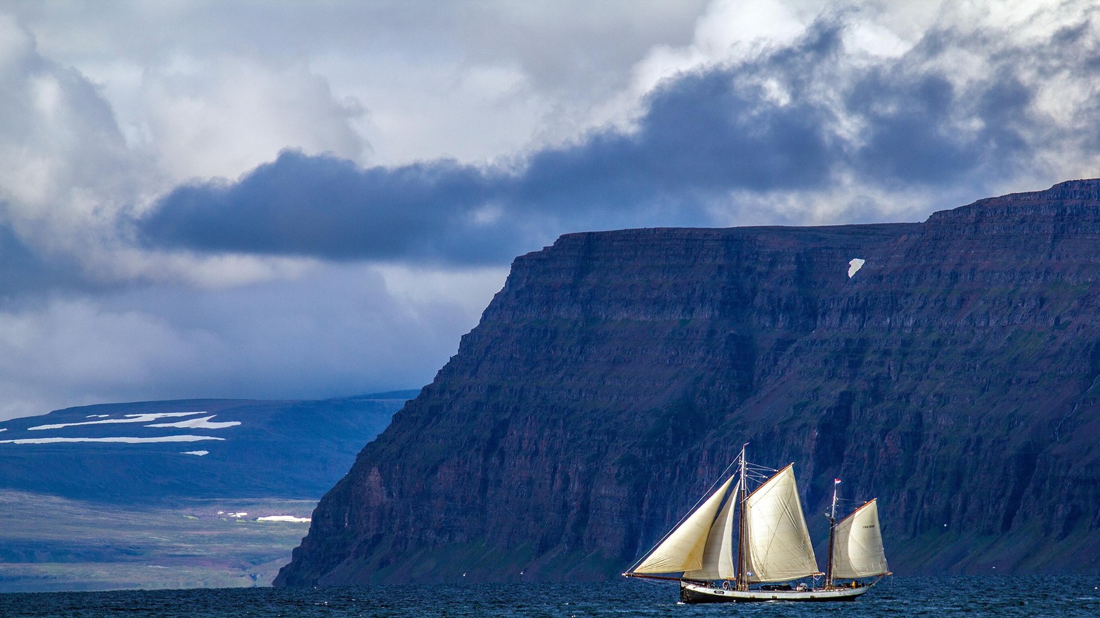 Arafed sailboat in the ocean with mountains in the background (water, watercraft, cloud, sail, mast)