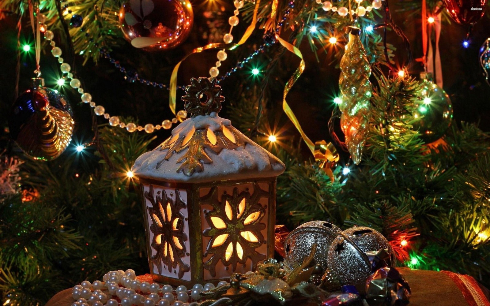 There is a small lantern on a table with ornaments and a tree (christmas day, christmas lights, holiday, christmas ornament, christmas)