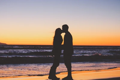 Pareja en silueta abrazándose al atardecer junto al océano