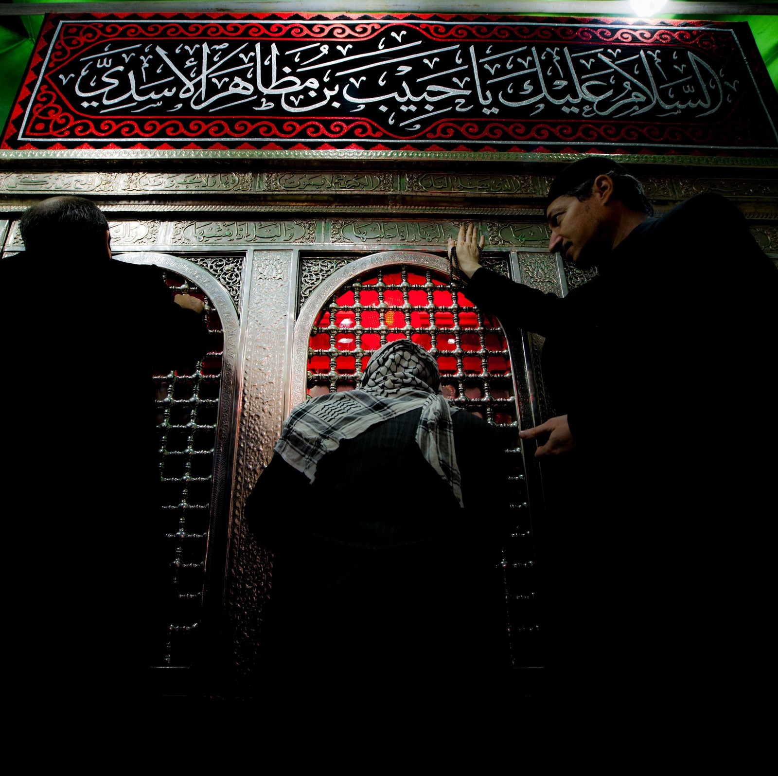 Muslim man and woman praying in front of a wall with a red and black design (arab, habib bin mothaher, love, peace, shia)