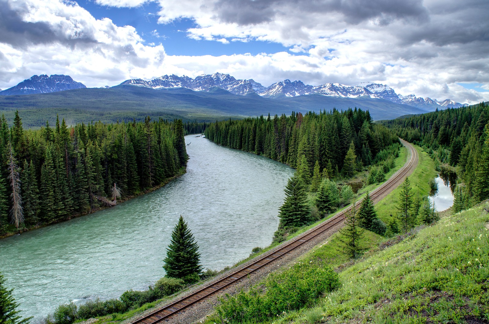 Arafed view of a train track running along a river with mountains in the background (rail transport, river, nature, mountain, wilderness)