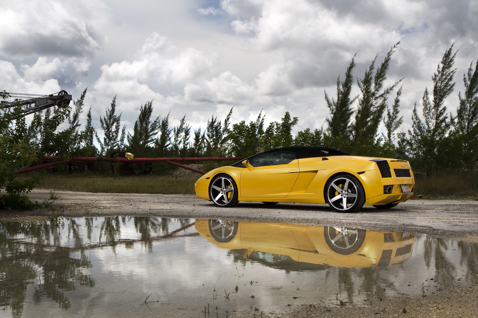 Carro esportivo amarelo estacionado em frente a um guindaste em uma estrada molhada (lamborghini, carro esportivo, carro, lamborghini gallardo spyder, supercarro)