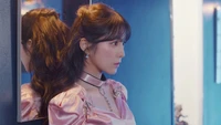 Irene de Red Velvet dans une tenue rose élégante, regardant pensivement dans un miroir, capturée dans un cadre bleu vibrant.