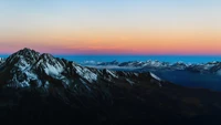 Montanhas cobertas de neve ao amanhecer com um céu em gradiente.