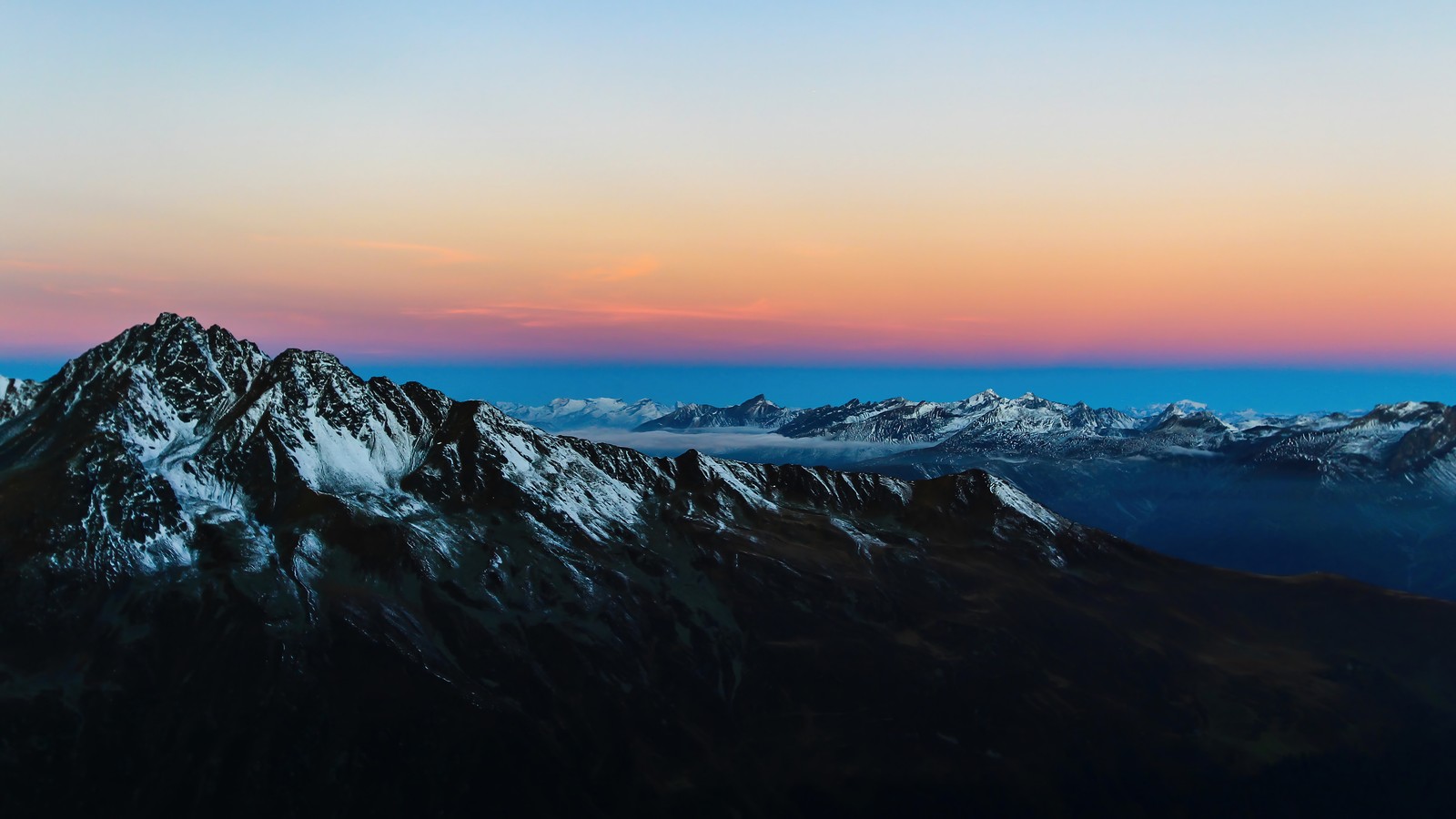 A view of a mountain range with a few snow covered mountains (mountain, mountains, snow, sunrise, scenery)