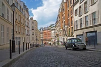 Charming cobblestone street with classic cars and historic buildings in a vibrant city neighborhood.