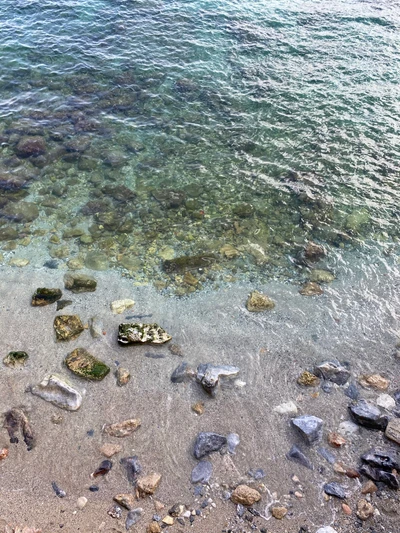 Aguas claras que revelan piedras de playa y materiales naturales