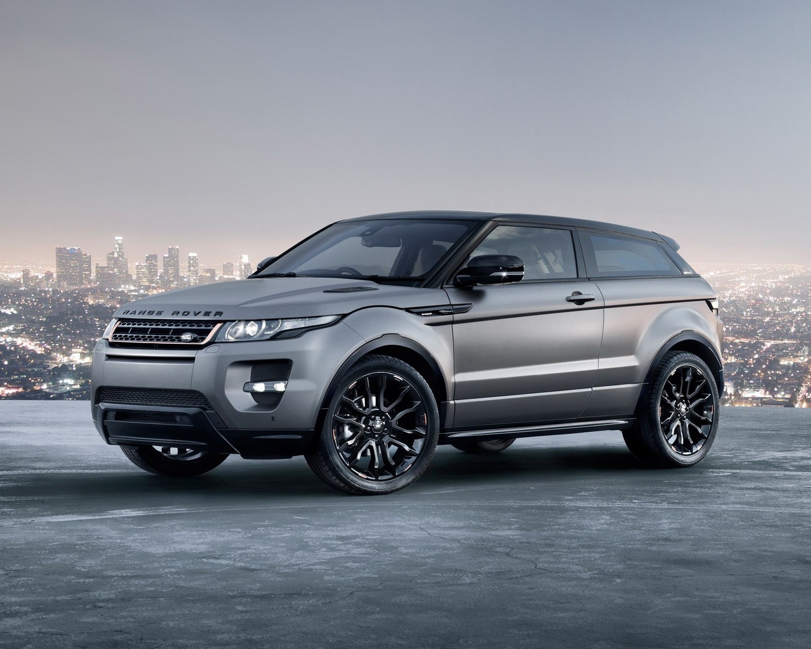 A silver range rover parked on a roof with city lights in the background (car, range rover)