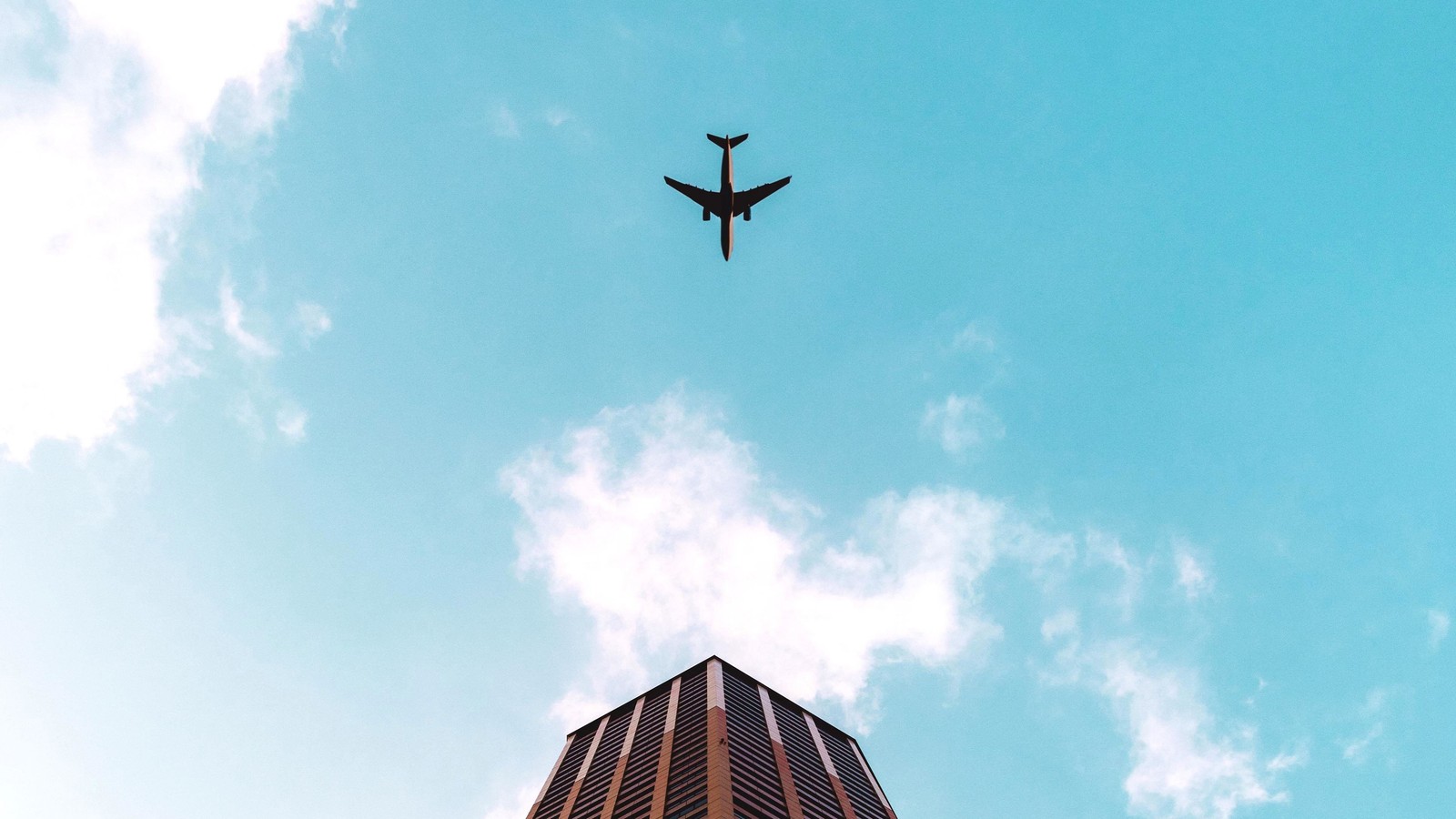 Un avion vole au-dessus d'un grand bâtiment dans le ciel (vol, avion, journée, nuage, architecture)