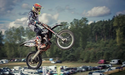 Pilote de motocross dynamique effectuant un stunt aérien sur fond de spectateurs et d'arbres.