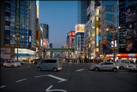 Vibrant cityscape at dusk featuring bustling traffic, illuminated skyscrapers, and pedestrians on a busy urban street.