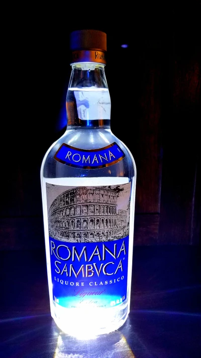 Glowing Bottle of Romana Sambuca Liquor Against Dark Background